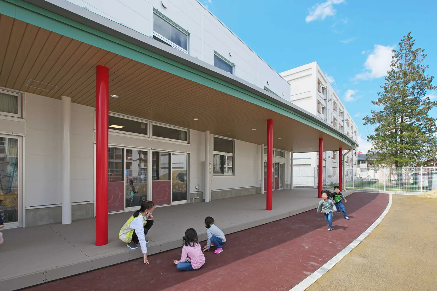 赤い柱のある園舎の前で遊ぶ子どもたち